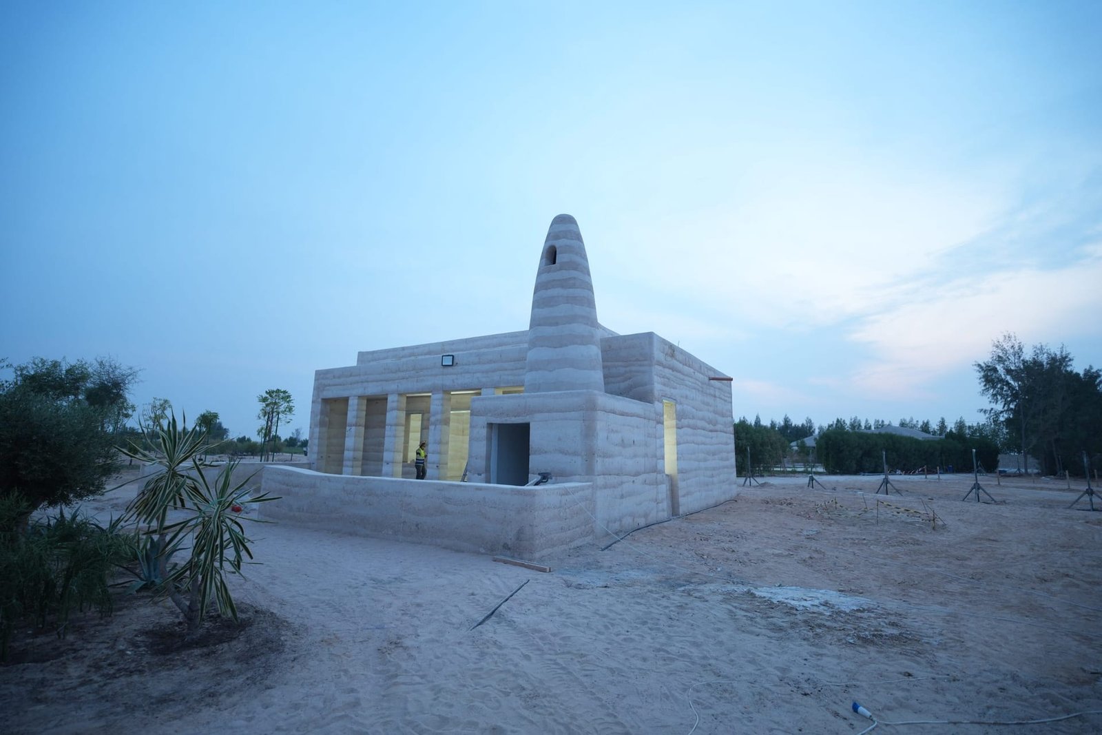 Rammed earth mosque with a layered conical minaret at Al Kaaban Resort, Qatar, at dusk