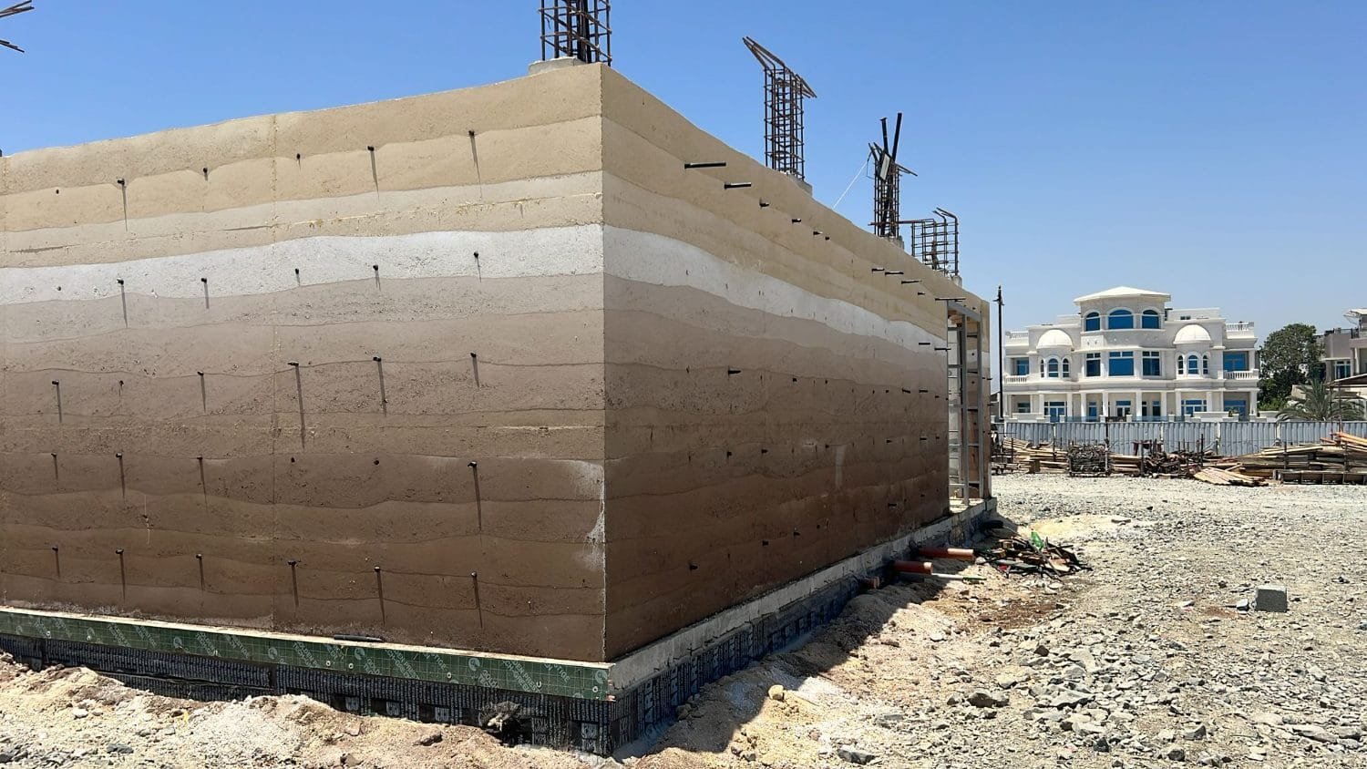 Completed in-situ stabilised rammed earth wall at Kalba Beach, Sharjah, tamped lifts banding cream to brown